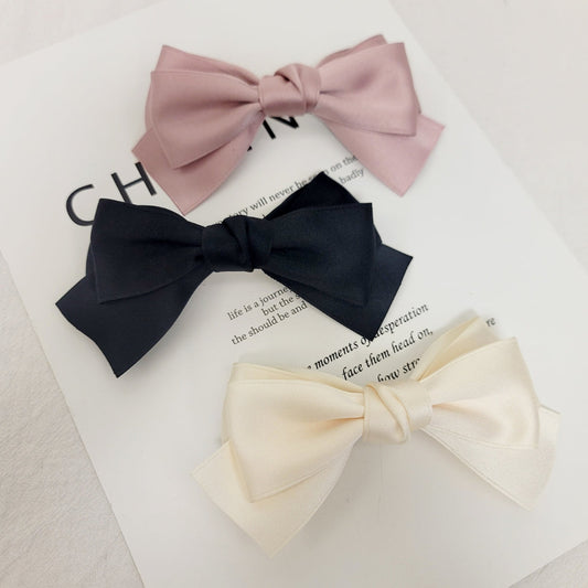 Three bow-shaped hair accessories in pink, black, and beige 